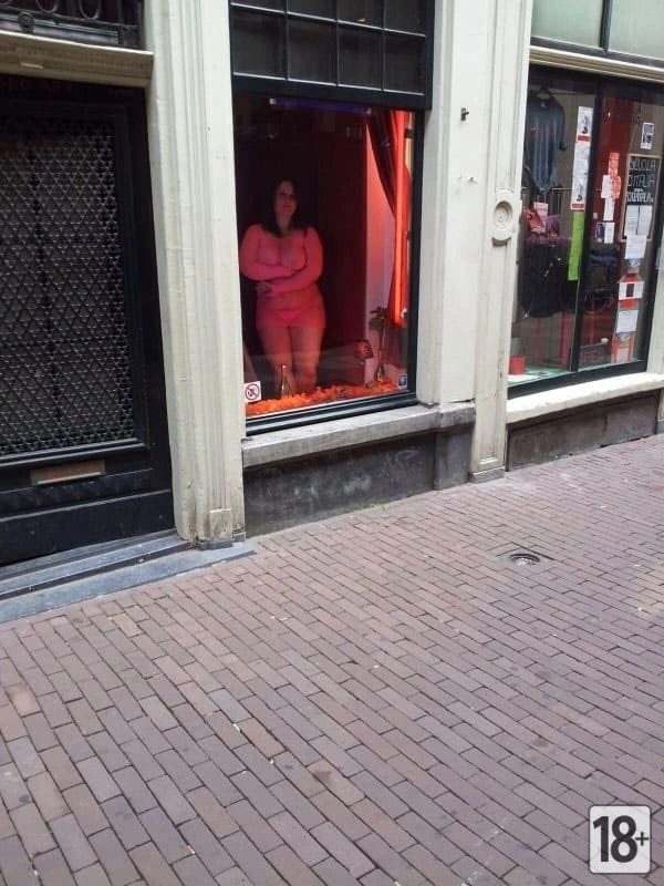 На витрине борделя проститутка привлекает внимание прохожих, приглашая их зайти внутрь.