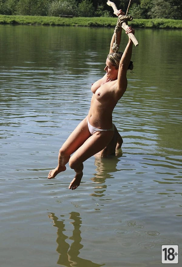 Фото: женщина-нудистка весело ныряет с тарзанки в озеро.